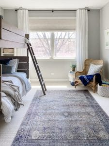 Boys bunk room features pretty Loloi Layla rug in olive charcoal, rattan chair from Wayfair, woven wood roman shades and white linen curtains, and Benjamin Moore harbor gray walls.