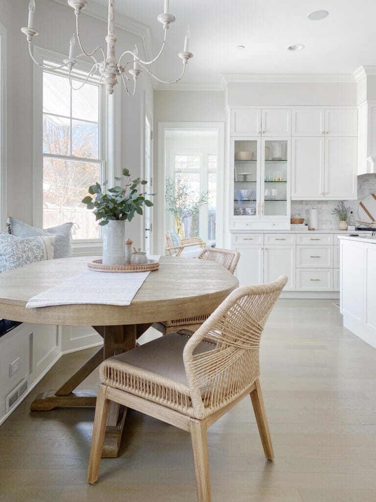 White kitchen features glass cabinets, banquette table with pretty woven chairs from Wayfair, antique inspired chandelier, and Benjamin Moore classic gray walls.