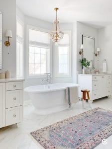 Bathroom features Caitlin Wilson vintage inspired runner, Serena & Lily dip dyed stool in tall, double vanities, pretty brass sconces and quartz countertops. Paint color is Benjamin Moore paper white.