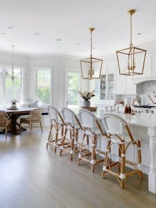 White kitchen features Serena & Lily Riviera stools in white, brass Darlana lanterns, quartz counters, white kitchen cabinets with a marble subway tile backsplash.