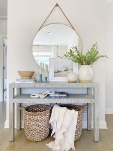 Serena & Lily Black raffia console table in fog, paired with a pretty round mirror and fresh spring styling.