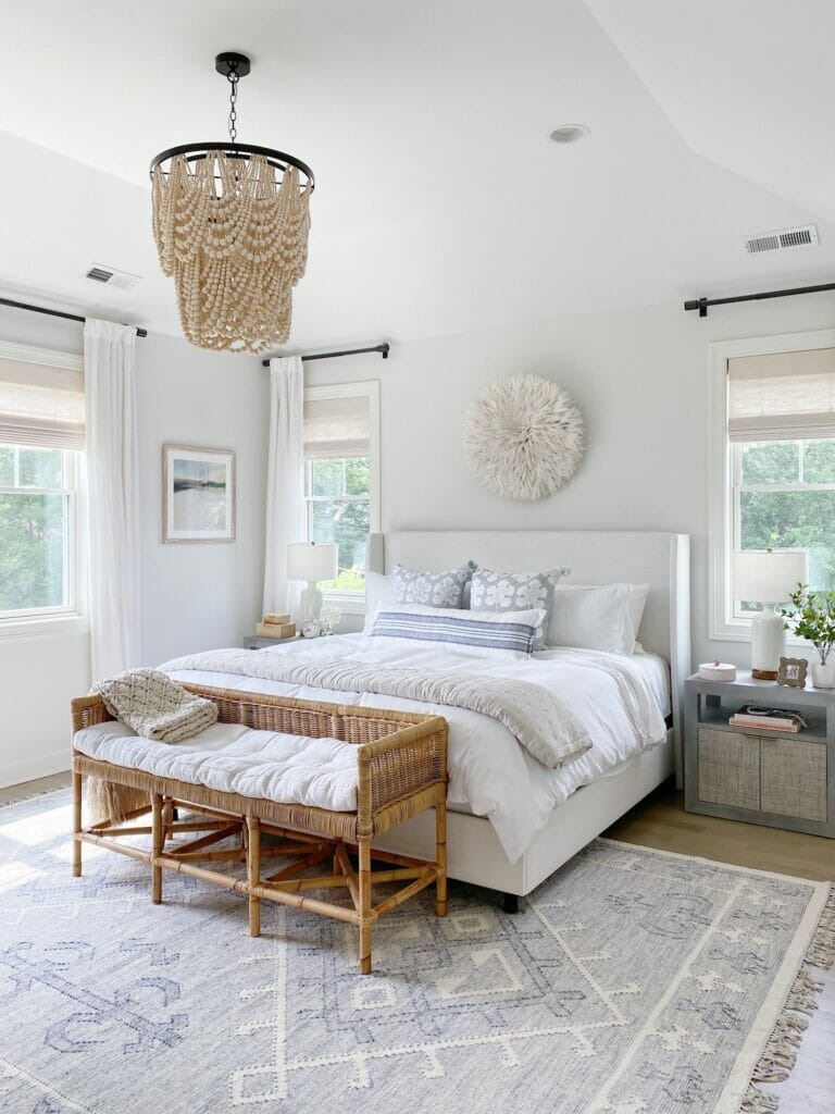 Coastal bedroom features upholstered bed, woven serena and lily bench, benjamin moore classic gray walls, beaded chandelier