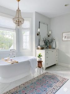 Primary bathroom with pretty vintage inspired rug, double vanities, brass chandelier over freestanding bathtub