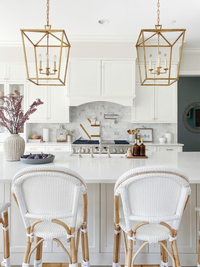 white kitchen features serena & lily riviera counter stools, brass lanterns, marble subway backsplash, quartz countertops and white kitchen cabinets
