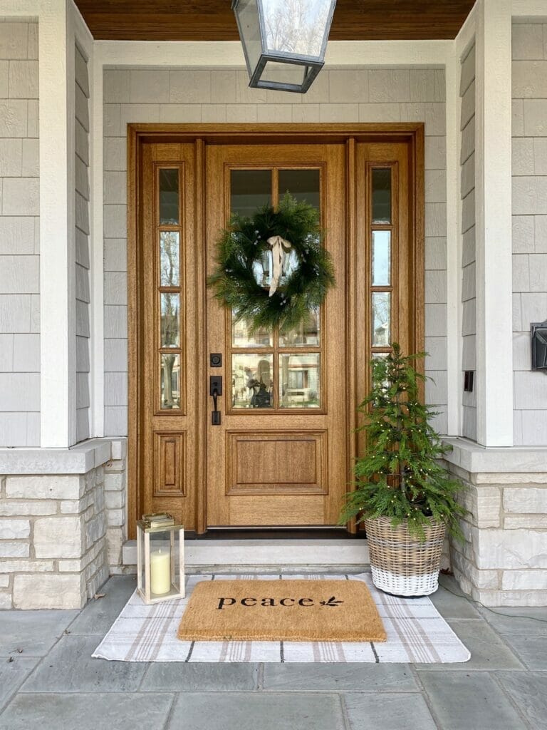 Christmas front porch features faux wreath, pre lit tree and cute christmas door mat