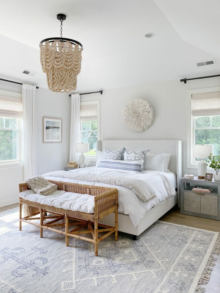 coastal inspired bedroom features upholstered bed, woven rattan nightstands, Serena & Lily alamere rug, and beaded chandelier